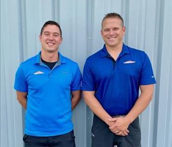 Two men in SERVPRO polos standing in front of a metal buidling
